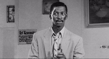 Movie still from “Hollywood Shuffle” (1987), directed by Robert Townsend – A black and white photo of a man in a suit holding a bottle; Close Up shot, Low angle