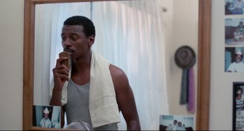 Movie still from “Hollywood Shuffle” (1987), directed by Robert Townsend – A man with a towel around his neck is brushing his teeth in the mirror; Close Up shot, Low angle
