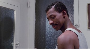Movie still from “Hollywood Shuffle” (1987), directed by Robert Townsend – A person in a bathroom near a wall; Close Up shot, Over the shoulder angle