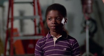 Movie still from “Hollywood Shuffle” (1987), directed by Robert Townsend – A young black boy wearing a purple and white striped shirt; Close Up shot, Over the shoulder angle