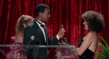 Movie still from “Hollywood Shuffle” (1987), directed by Robert Townsend – A man in a tuxedo holding a trophy; Medium shot, Low angle