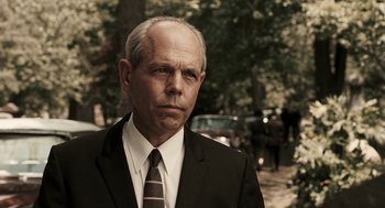 Movie still from “Hollywoodland” (2006), directed by Allen Coulter – An older man wearing a suit and tie in front of trees; Close Up shot, Over the shoulder angle