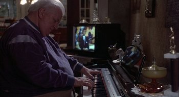 Movie still from “Home for the Holidays” (1995), directed by Jodie Foster – An older man playing the piano in front of a television; Medium shot, High angle