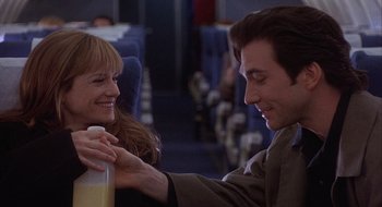 Movie still from “Home for the Holidays” (1995), directed by Jodie Foster – A man and a woman are smiling at each other on a plane; Medium shot, Low angle