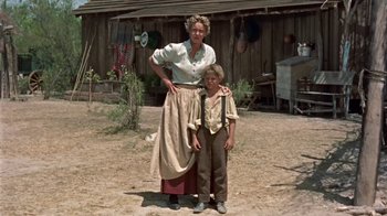Movie still from “Hondo” (1953), directed by John Farrow – An older woman standing next to a young boy in front of a house; Wide shot, Low angle