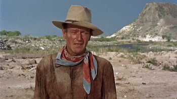 Movie still from “Hondo” (1953), directed by John Farrow – A man wearing a cowboy hat standing in the desert; Medium shot, Over the shoulder angle