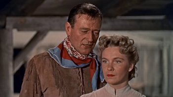 Movie still from “Hondo” (1953), directed by John Farrow – A man and a woman standing next to each other; Medium shot, Low angle