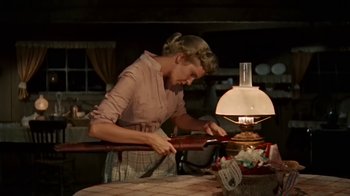 Movie still from “Hondo” (1953), directed by John Farrow – A woman in a brown shirt is cutting paper with an electric knife; Medium shot, Low angle