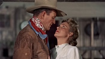 Movie still from “Hondo” (1953), directed by John Farrow – A man and a woman standing next to each other; Medium shot, Low angle