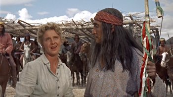 Movie still from “Hondo” (1953), directed by John Farrow – A man and a woman standing next to each other in front of horses; Medium shot, Over the shoulder angle