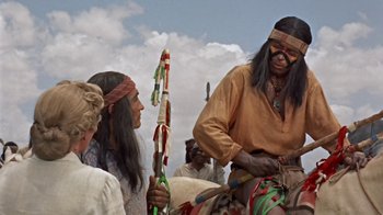 Movie still from “Hondo” (1953), directed by John Farrow – Two native american women and a man in traditional clothing; Medium shot, Over the shoulder angle