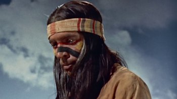 Movie still from “Hondo” (1953), directed by John Farrow – A man with long black hair and a face paint; Close Up shot, Low angle