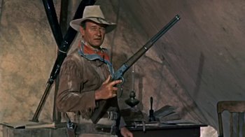 Movie still from “Hondo” (1953), directed by John Farrow – A man holding a rifle in a room; Medium shot, Low angle