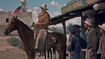 Movie still from “Hondo” (1953), directed by John Farrow – A man on a horse in front of two other men; Wide shot, Low angle