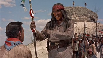 Movie still from “Hondo” (1953), directed by John Farrow – An old man holding a spear in front of a group of people; Medium shot, Over the shoulder angle
