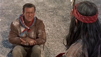 Movie still from “Hondo” (1953), directed by John Farrow – A man sitting on the ground next to a woman; Medium shot, Over the shoulder angle