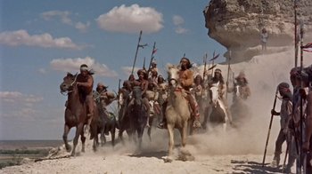 Movie still from “Hondo” (1953), directed by John Farrow – A group of people on horseback riding through the desert; Wide shot, Low angle