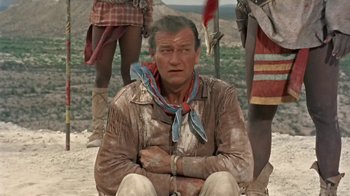 Movie still from “Hondo” (1953), directed by John Farrow – A man sitting on the ground wearing a cowboy outfit; Medium shot, High angle