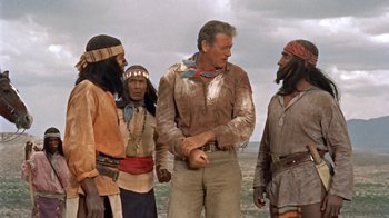 Movie still from “Hondo” (1953), directed by John Farrow – A group of men standing next to each other on a beach; Medium shot, Over the shoulder angle