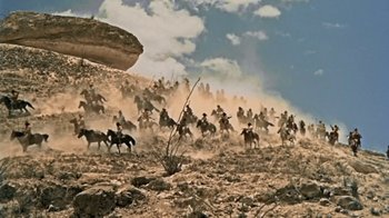Movie still from “Hondo” (1953), directed by John Farrow – A group of people riding horses through a field; Extreme Wide shot, Low angle