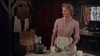Movie still from “Hondo” (1953), directed by John Farrow – A woman standing at a table with a plate in front of it; Medium shot, Low angle