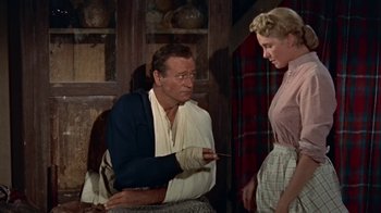 Movie still from “Hondo” (1953), directed by John Farrow – A man and a woman are standing in front of a window; Medium shot, Low angle
