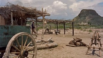 Movie still from “Hondo” (1953), directed by John Farrow – A man walking on a dirt road near a wooden structure; Extreme Wide shot, Low angle