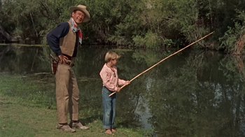 Movie still from “Hondo” (1953), directed by John Farrow – A man and a boy fishing in a pond; Wide shot, Over the shoulder angle