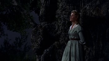 Movie still from “Hondo” (1953), directed by John Farrow – A woman standing next to a tree at night; Medium shot, Low angle