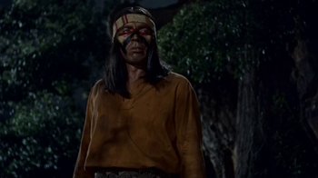 Movie still from “Hondo” (1953), directed by John Farrow – A man with a face paint standing next to a tree; Medium shot, Low angle