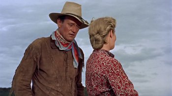 Movie still from “Hondo” (1953), directed by John Farrow – A man and a woman standing next to each other in front of a cloudy sky; Medium shot, Low angle