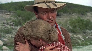 Movie still from “Hondo” (1953), directed by John Farrow – A man and a woman are hugging in a field; Close Up shot, Over the shoulder angle