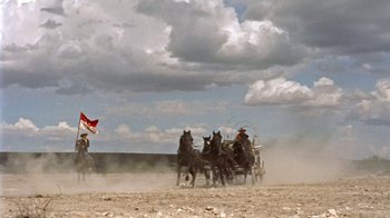 Movie still from “Hondo” (1953), directed by John Farrow – A group of horses pulling a carriage down a dirt road; Extreme Wide shot, Low angle