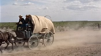 Movie still from “Hondo” (1953), directed by John Farrow – A covered wagon traveling down a dirt road; Wide shot, Low angle