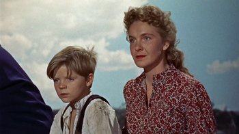 Movie still from “Hondo” (1953), directed by John Farrow – A woman standing next to a young boy in a field; Medium shot, Low angle