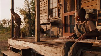Movie still from “Honeydripper” (2007), directed by John Sayles – A man sitting on a porch of a wooden house; Wide shot, Low angle