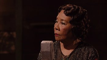 Movie still from “Honeydripper” (2007), directed by John Sayles – An older woman is sitting in front of a microphone; Close Up shot, High angle