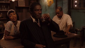 Movie still from “Honeydripper” (2007), directed by John Sayles – A man in a suit drinking a beverage; Medium shot, Over the shoulder angle