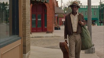 Movie still from “Honeydripper” (2007), directed by John Sayles – A man walking down the street with a guitar case; Medium shot, Over the shoulder angle