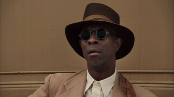 Movie still from “Honeydripper” (2007), directed by John Sayles – A man wearing a hat and sunglasses with a brown suit; Close Up shot, Low angle
