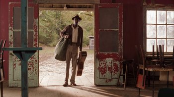 Movie still from “Honeydripper” (2007), directed by John Sayles – A man standing in front of an open door holding luggage; Wide shot, Over the shoulder angle