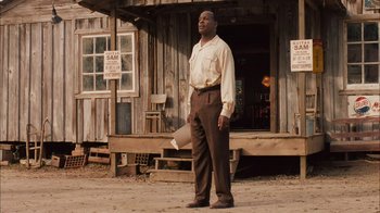 Movie still from “Honeydripper” (2007), directed by John Sayles – A man standing in front of a building holding a paper; Medium shot, Low angle