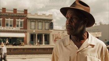 Movie still from “Honeydripper” (2007), directed by John Sayles – An older man wearing a brown hat standing in front of a building; Close Up shot, Over the shoulder angle