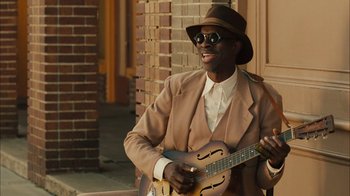 Movie still from “Honeydripper” (2007), directed by John Sayles – A man in a hat and sunglasses playing a guitar; Medium shot, Over the shoulder angle