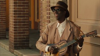 Movie still from “Honeydripper” (2007), directed by John Sayles – A man in a hat and sunglasses holding a guitar; Medium shot, High angle