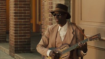 Movie still from “Honeydripper” (2007), directed by John Sayles – A man in a hat and sunglasses playing a guitar; Medium shot, Over the shoulder angle