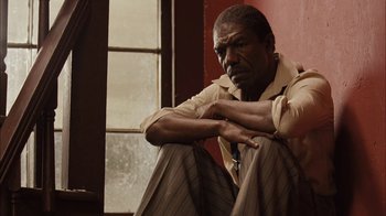 Movie still from “Honeydripper” (2007), directed by John Sayles – A man sitting in front of a window with his arms crossed; Medium shot, Low angle