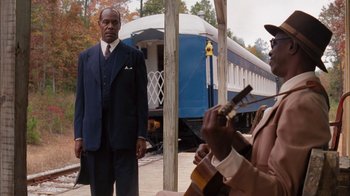 Movie still from “Honeydripper” (2007), directed by John Sayles – A man standing next to another man playing a guitar; Medium shot, Over the shoulder angle
