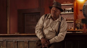 Movie still from “Honeydripper” (2007), directed by John Sayles – A man sitting on a bench wearing a hat; Medium shot, Low angle