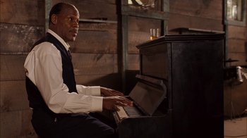 Movie still from “Honeydripper” (2007), directed by John Sayles – A man sitting in front of an old fashioned piano; Medium shot, Low angle
